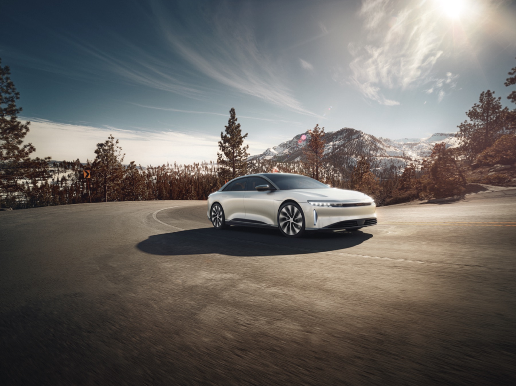 Lucid Air on a mountain road above Tahoe, snow-covered peaks behind